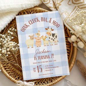 K&ouml;nnte beinhalten: Eine blau-wei&szlig; karierte Einladung mit dem Text "Oink, Cluck, Baa, & Moo" und "Jackson wird 2!" zeigt Illustrationen von Hoftieren. Die Einladung liegt auf einem Weidenkorb mit getrockneten Blumen.