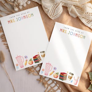 May include: Two white rectangular stationery sheets featuring the text FROM THE DESK OF MRS. JOHNSON in multicolored letters at the top. The bottom borders display watercolor illustrations of a pink tumbler, pencil, apple, books, and coffee cup.