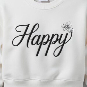 Peut inclure: Sweat-shirt crème avec le mot "Happy" brodé en noir en écriture cursive. Un petit motif floral noir est présent à côté du mot. Le sweat-shirt a un col rond et une apparence décontractée.