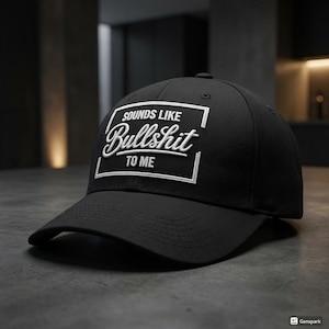 May include: Black baseball cap featuring the embroidered phrase "SOUNDS LIKE Bullshit TO ME" in white, within a white rectangular frame. The cap has a curved peak and a structured crown.
