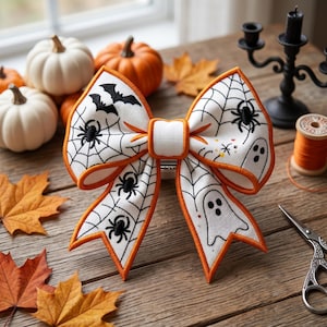Pode incluir: Um grande laço decorativo de Halloween com fundo branco, teias de aranha pretas, aranhas, morcegos e fantasmas. O laço tem uma borda laranja. Abóboras e folhas de outono ao fundo.