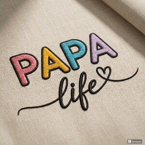 Peut inclure: Broderie sur tissu beige. Le mot "PAPA" est écrit en lettres colorées : rose, jaune, bleu et violet. En dessous, le mot "life" est écrit en cursive, avec un symbole de cœur. Le design est probablement pour un cadeau ou une décoration intérieure.