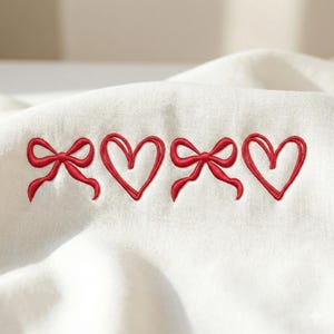 May include: A white fabric with embroidered red bows and hearts. The design features two bows and two hearts in a row, creating a charming and romantic pattern. The embroidery is detailed and adds a touch of elegance.