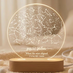 Puede incluir: Una lámpara de noche redonda e iluminada con un mapa de constelaciones. La lámpara tiene una base de madera y una parte superior redonda y transparente con un patrón de estrellas y el texto "Jess & Jordan" y "When the stars aligned". También incluye la fecha "17 at may 2018 | Ammcin".