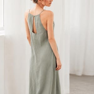 Könnte beinhalten: Ein ärmelloses Maxikleid in Salbeigrün mit hohem Ausschnitt, dünnen Spaghettiträgern und einem Schlüsselloch-Ausschnitt am oberen Rücken. Das Kleidungsstück hat eine lockere, bodenlange Silhouette mit geradem Saum und einer matten Oberfläche.