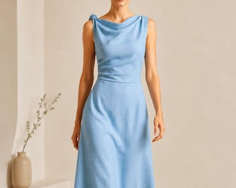 May include: A sleeveless, light blue dress with a draped neckline and a fitted waist. The dress has a midi-length skirt and is worn with strappy sandals. The dress features a bow detail on the shoulder.