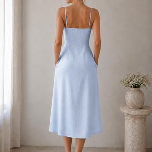 May include: A light blue midi dress with thin spaghetti straps, a fitted bodice, and a flared skirt. The dress features a straight neckline, a defined waistline, and side pockets, shown from the back view with a simple, solid-colored design.