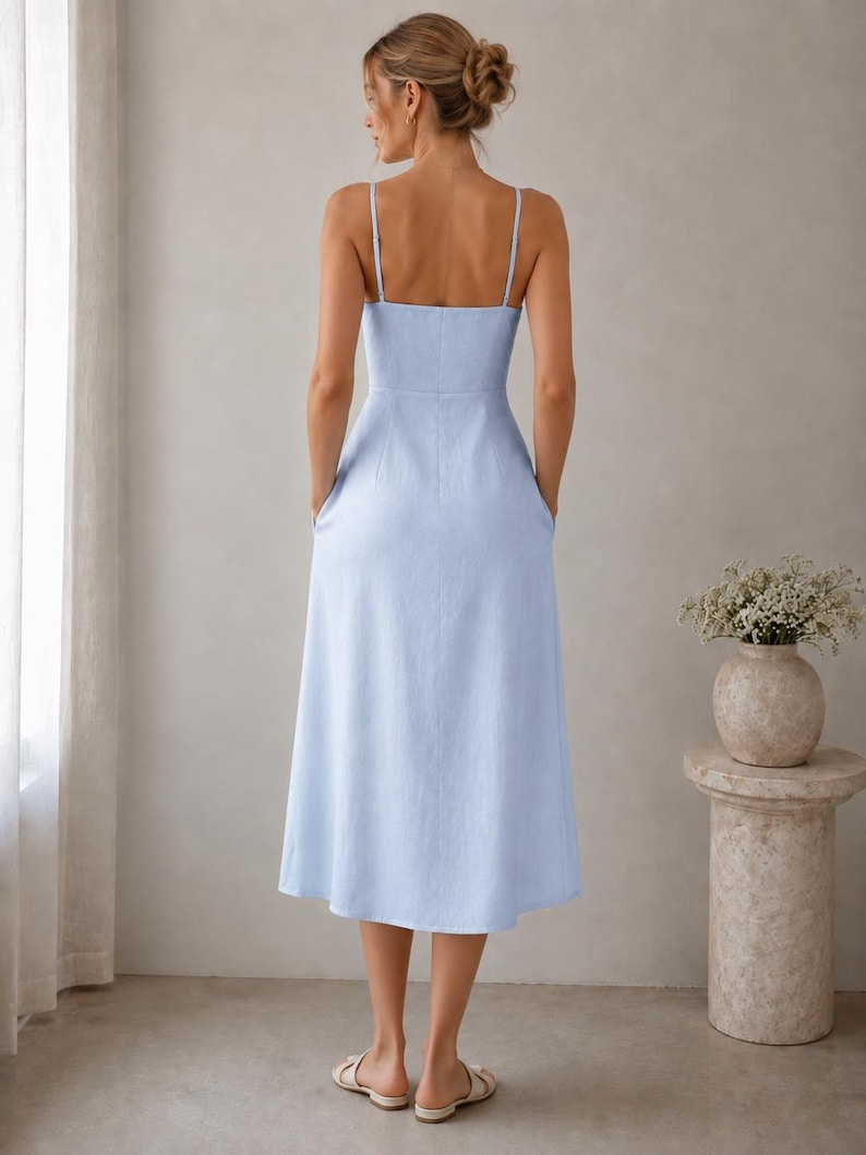 May include: A light blue midi dress with thin spaghetti straps, a fitted bodice, and a flared skirt. The dress features a straight neckline, a defined waistline, and side pockets, shown from the back view with a simple, solid-colored design.