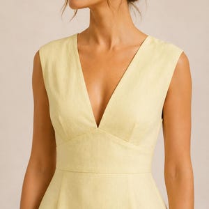 Puede incluir: Un vestido sin mangas de color amarillo p&aacute;lido con un escote en V profundo, un corpi&ntilde;o ajustado con una costura definida en la cintura y un acabado de tela texturizada. La prenda tiene tirantes anchos y una silueta estructurada y limpia.