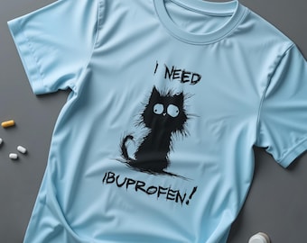 Op de afbeelding: Lichtblauw t-shirt met een zwarte cartoonkat en de tekst "I NEED IBUPROFEN!". De kat heeft een geschrokken uitdrukking. Er liggen meerdere pillen rond het shirt.