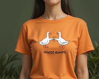 May include: Orange t-shirt featuring a cartoon design of two white geese bumping beaks, with the text "GOOSE BUMPS" below. The geese have orange feet and beaks. The shirt is a solid orange color.