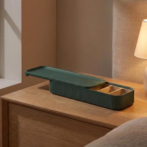 Green pill holder, shown open on a wooden bedside table next to a lamp.