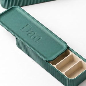 Green pill holder with “Dan” embossed on the lid, shown open with compartments inside.