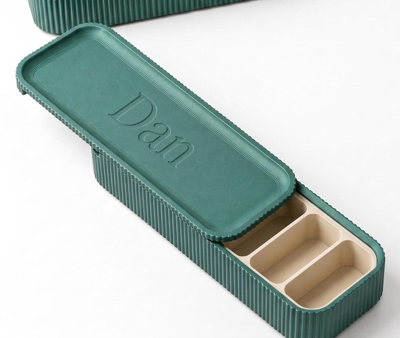 Green pill holder with “Dan” embossed on the lid, shown open with compartments inside.