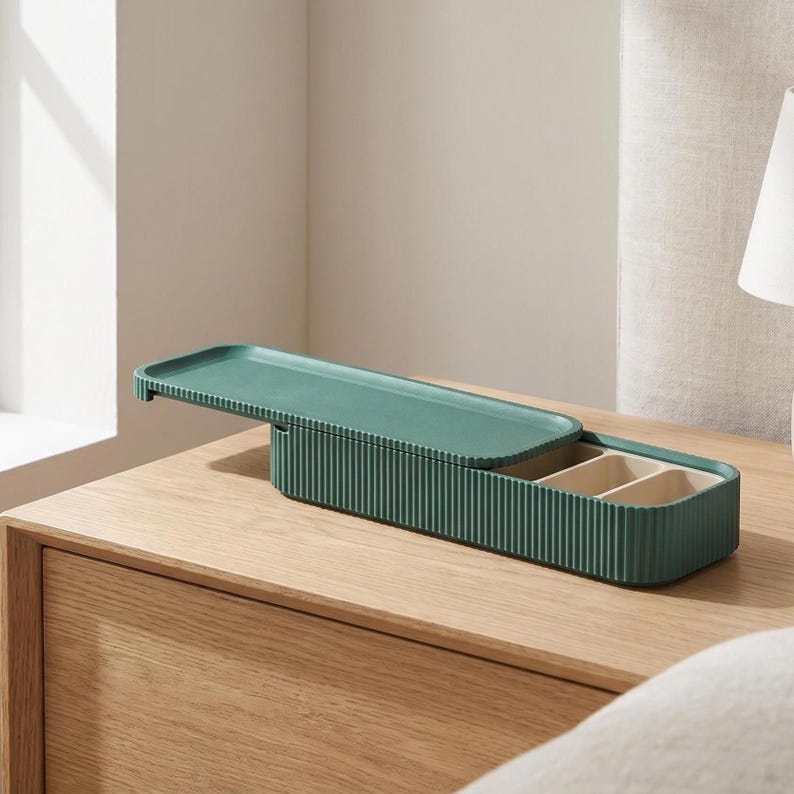 Green ribbed pill holder with sliding lid, placed open on a wooden bedside table next to a lamp.