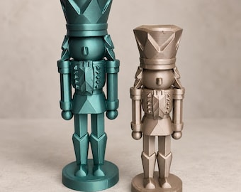 May include: Two standing nutcracker figurines with a geometric, faceted design. The taller figure is a metallic teal color, while the shorter figure is a metallic champagne gold color. Both feature a tall hat, uniform jacket, and circular base.