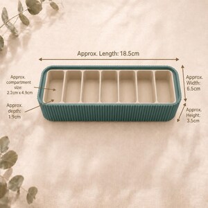 Oxide Green Metallic and beige large pill case shown open, with approximate length, width, height, compartment size and depth measurements labelled on a soft neutral background.