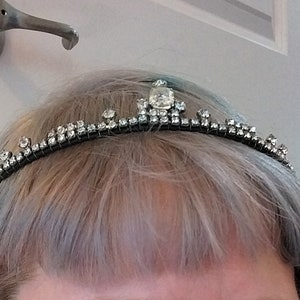 May include: A person with blue and grey hair is wearing a silver tiara with rhinestones. They are smiling and have a silver nose ring with a blue gemstone.