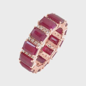 May include: A rose gold ring featuring rectangular, deep red gemstones and small, clear accent stones. The ring's design showcases a continuous pattern of alternating gemstones and accent stones, creating a luxurious and elegant look.
