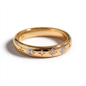 Può includere: Un anello a fascia in oro lucido caratterizzato da una serie di pietre rotonde trasparenti alternate a incisioni a forma di stella a quattro punte. La superficie metallica liscia e arrotondata riflette la luce, mettendo in risalto le gemme.