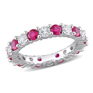 May include: A silver ring featuring alternating round and oval-cut gemstones. The ring showcases vibrant red rubies and sparkling white diamonds, set in a continuous band. The gemstones are securely held by small, round prongs.
