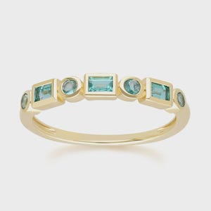 Könnte beinhalten: Ein goldener Ring mit einer Reihe abwechselnder geometrischer Formen. Der Ring hat ein poliertes Goldband und ist mit rechteckigen, quadratischen und runden hellblauen Edelsteinen verziert. Die Edelsteine sind gleichmäßig um den Ring herum angeordnet.