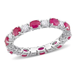 May include: A silver ring featuring a continuous row of oval-cut, vibrant red rubies and interspersed with small, round, clear diamonds. The ring's band is a polished silver, creating a striking contrast with the gemstones.
