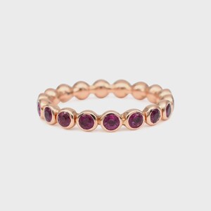 May include: Rose gold ring featuring a series of round, deep red gemstones. The gemstones are evenly spaced around the band, creating a continuous pattern. The ring has a polished finish and a classic, elegant design.