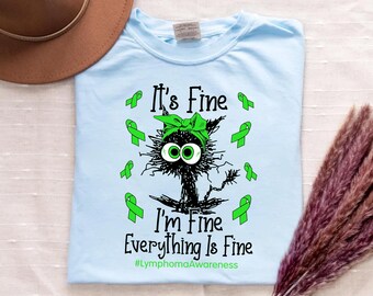 May include: Pale blue t-shirt with a cartoon black cat wearing a green bow and green eyes. The text reads "It's Fine, I'm Fine, Everything Is Fine" and "#LymphomaAwareness" in green.