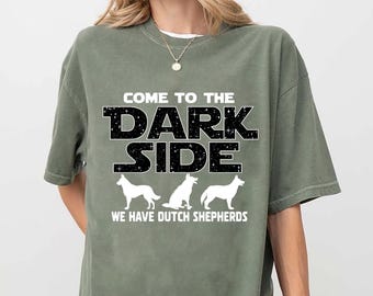 May include: An olive green t-shirt featuring the text "COME TO THE DARK SIDE" in black with white stars. Below the text are three white Dutch Shepherd dog silhouettes, and the text "WE HAVE DUTCH SHEPHERDS".