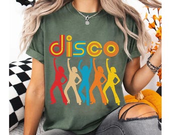 May include: An olive green t-shirt with the word "DISCO" in colorful retro lettering. Below the word are five dancing figures in red, tan, blue, orange, and yellow, with arms raised.
