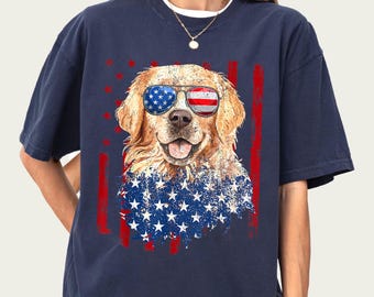 May include: Navy blue t-shirt with a golden retriever wearing sunglasses in the style of the American flag. The dog has a patriotic design on its chest, with red stripes and white stars. The shirt has a crew neck.