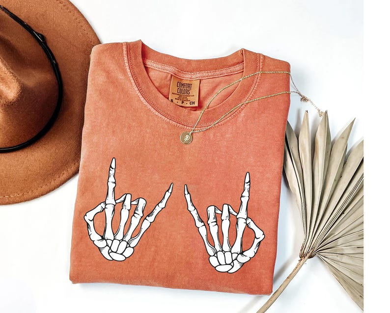 a red t-shirt with a graphic of two skeletal hands making a "rock on" sign, along with a brown hat and a fan.