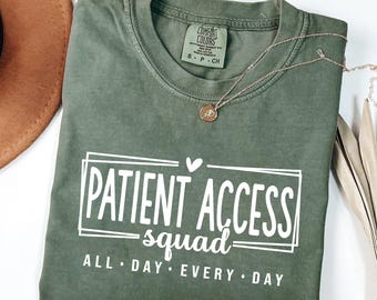 May include: An olive green crew neck t-shirt with a white graphic print that reads PATIENT ACCESS squad ALL DAY EVERY DAY inside a rectangular frame with a small heart icon. The shirt features a Comfort Colors brand label at the inner neckline.