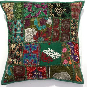 May include: Square patchwork cushion with a green border. The cushion features a variety of embroidered fabric squares in shades of green, purple, red, and gold. The design includes floral and geometric patterns.