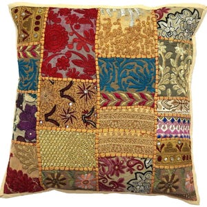 May include: Square decorative pillow with a patchwork design. The pillow features various embroidered and embellished fabric squares in shades of red, gold, blue, and purple. The edges are trimmed with a light beige border.