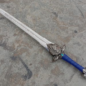 May include: A decorative sword with a silver blade and ornate hilt. The blade has the inscription "You are my anchor; I am Your Compass." The handle is wrapped in blue material, and the hilt features a turquoise gem.