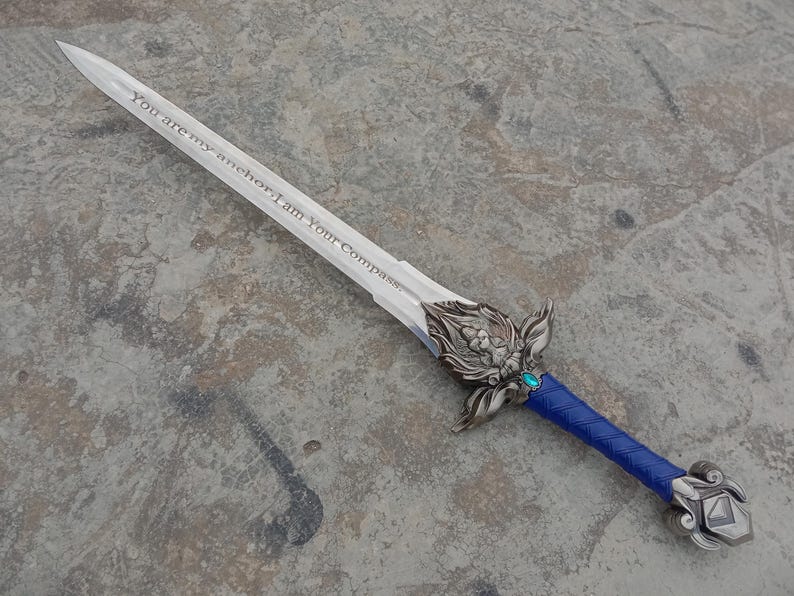 May include: A decorative sword with a silver blade and ornate hilt. The blade has the inscription "You are my anchor; I am Your Compass." The handle is wrapped in blue material, and the hilt features a turquoise gem.