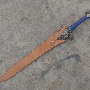 May include: A decorative sword with a blue wrapped handle and ornate silver hilt. The blade is sheathed in a brown leather scabbard. A small, round, blue gem is set near the hilt.
