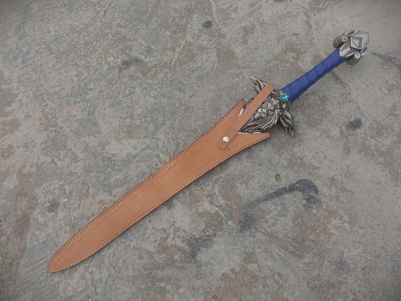 May include: A decorative sword with a blue wrapped handle and ornate silver hilt. The blade is sheathed in a brown leather scabbard. A small, round, blue gem is set near the hilt.