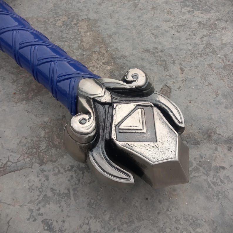 May include: Close-up of a sword hilt and handle. The handle is wrapped in blue material with a textured pattern. The hilt is silver-colored with ornate, swirling designs and a geometric center.
