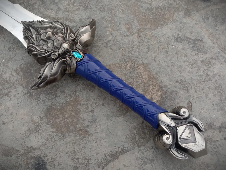 May include: A detailed fantasy sword with a silver blade and ornate metalwork. The hilt features a blue, textured grip and a decorative guard with a teal-colored gem. The sword's design is intricate and detailed.
