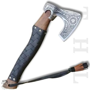 May include: A Viking-style axe with a silver-colored head featuring intricate engraved patterns and a wooden handle. The handle is wrapped in black leather with a braided design. A leather strap with a tassel is attached.