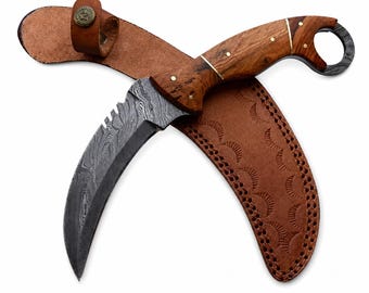 Può includere: Un coltello karambit curvo con lama in acciaio Damasco dal motivo ondulato, manico in legno con perni in ottone e un anello per il dito sul pomolo. È accompagnato da un fodero in pelle marrone con un motivo a mezzaluna stampato e un bottone.