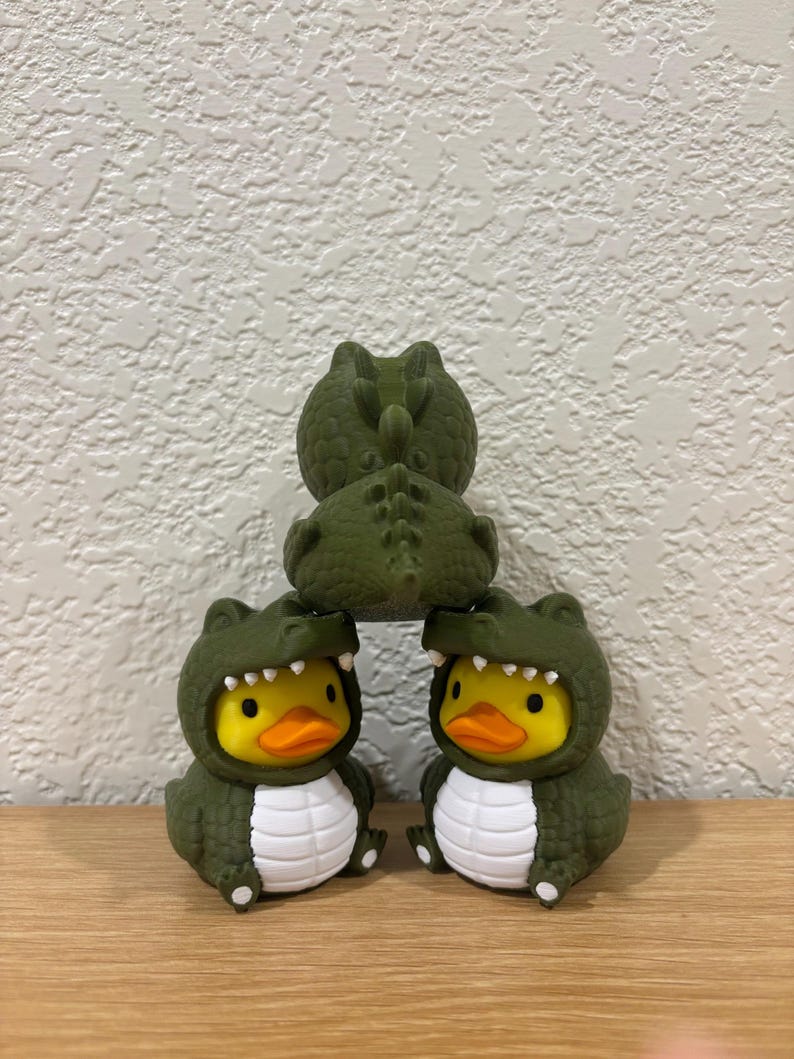 Puede incluir: Tres patos de goma amarillos con disfraces de caim&aacute;n verde oscuro, dientes blancos y escamas blancas en el vientre. Los dos patos inferiores est&aacute;n uno al lado del otro, mientras que el tercero est&aacute; encima, mostrando su espalda y cola.