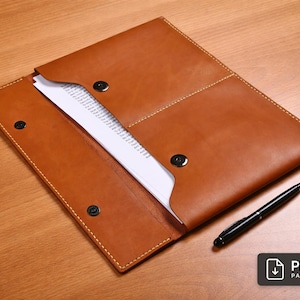 May include: A brown leather document holder with a snap closure, holding white papers. A black pen rests beside it on a wooden surface. The PDF pattern icon is in the bottom right corner.