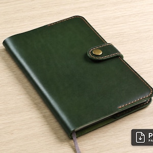 May include: A dark green notebook cover featuring a smooth finish, contrasting brown stitching along the edges, and a secure strap closure with a round brass-colored metal snap button. A small gray ribbon bookmark extends from the bottom edge.