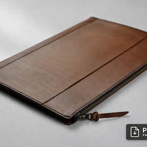 Puede incluir: Un portadocumentos de cuero marrón con forma rectangular y esquinas redondeadas, costuras visibles en los bordes y un cierre de cremallera metálico con una lengüeta de cuero a juego. Se observa un pequeño icono negro con el texto PDF PATTERN.