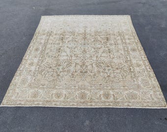 May include: A rectangular, beige-colored rug with an intricate floral pattern. The rug has a central design with a border featuring floral and geometric elements. The rug is placed on a dark gray surface.