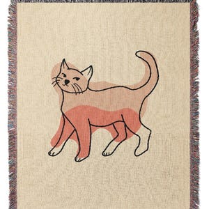 K&ouml;nnte beinhalten: Beige Decke mit einer Katzenillustration. Die Katze ist schwarz umrandet mit Pfirsich- und Korallent&ouml;nen. Die Decke hat einen Fransenrand mit verschiedenen Farben.